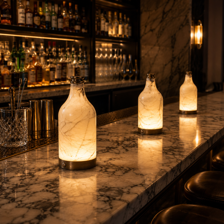 Decorative bottles with a warm glow on a marble bar counter with a bar in the background.