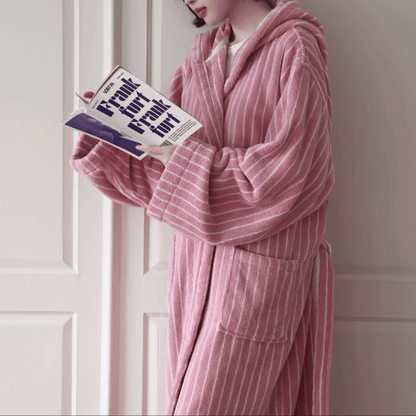 Person wearing a pink striped robe holding a book in a room with white paneled walls.