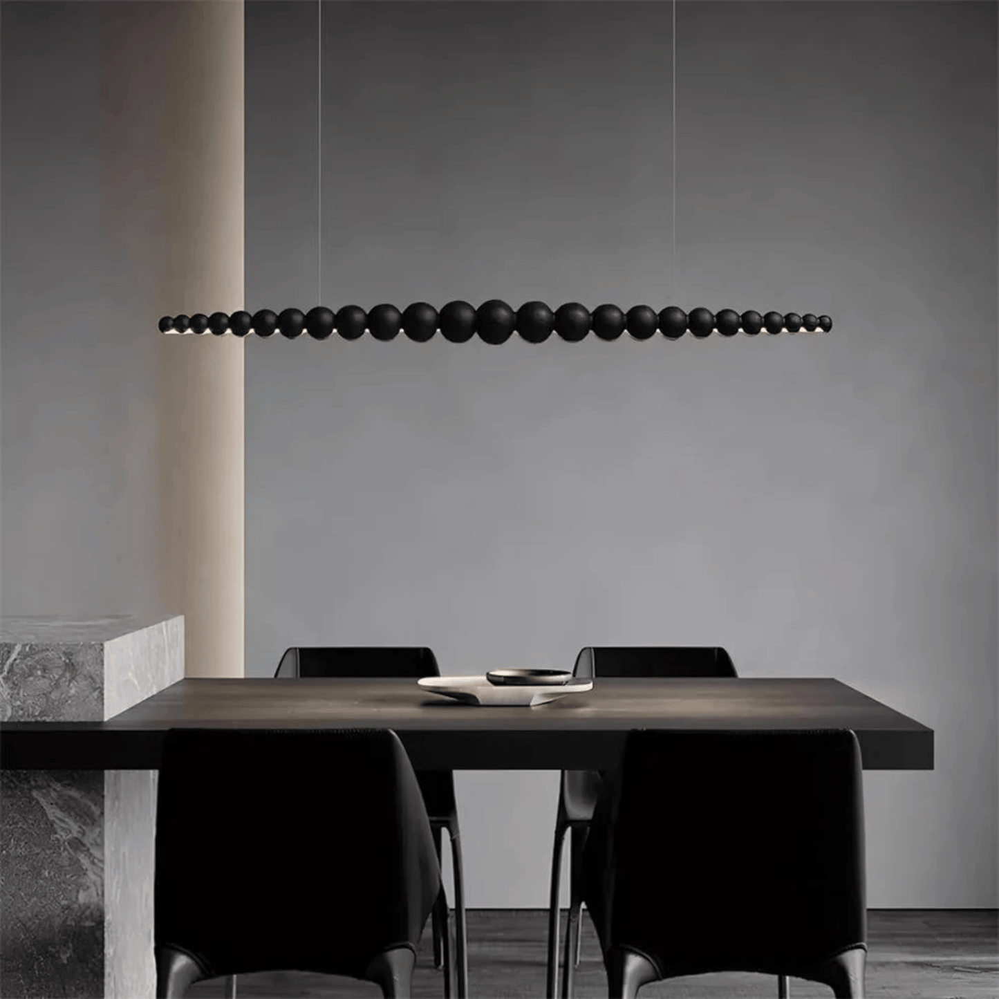 Modern dining area with a long, dark pendant light fixture hanging above a table and chairs.