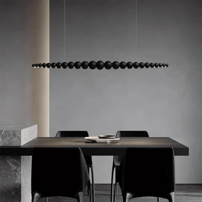 Modern dining area with a long, dark pendant light fixture hanging above a table and chairs.