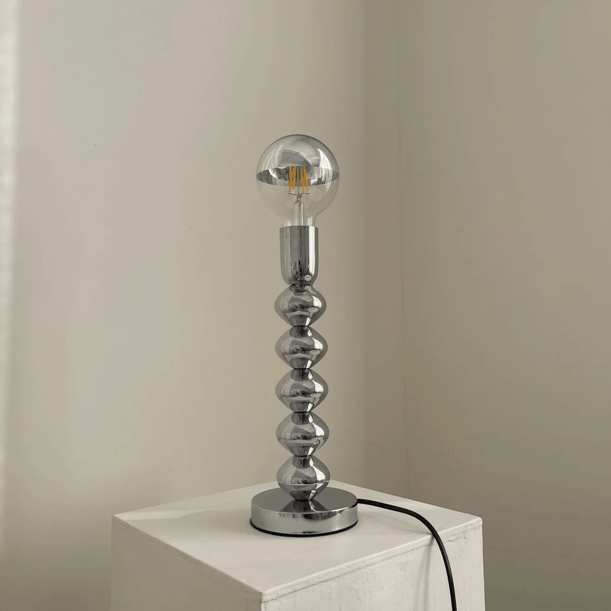 Silver table lamp with a unique design on a white surface against a beige wall.