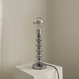 Silver table lamp with a unique design on a white surface against a beige wall.
