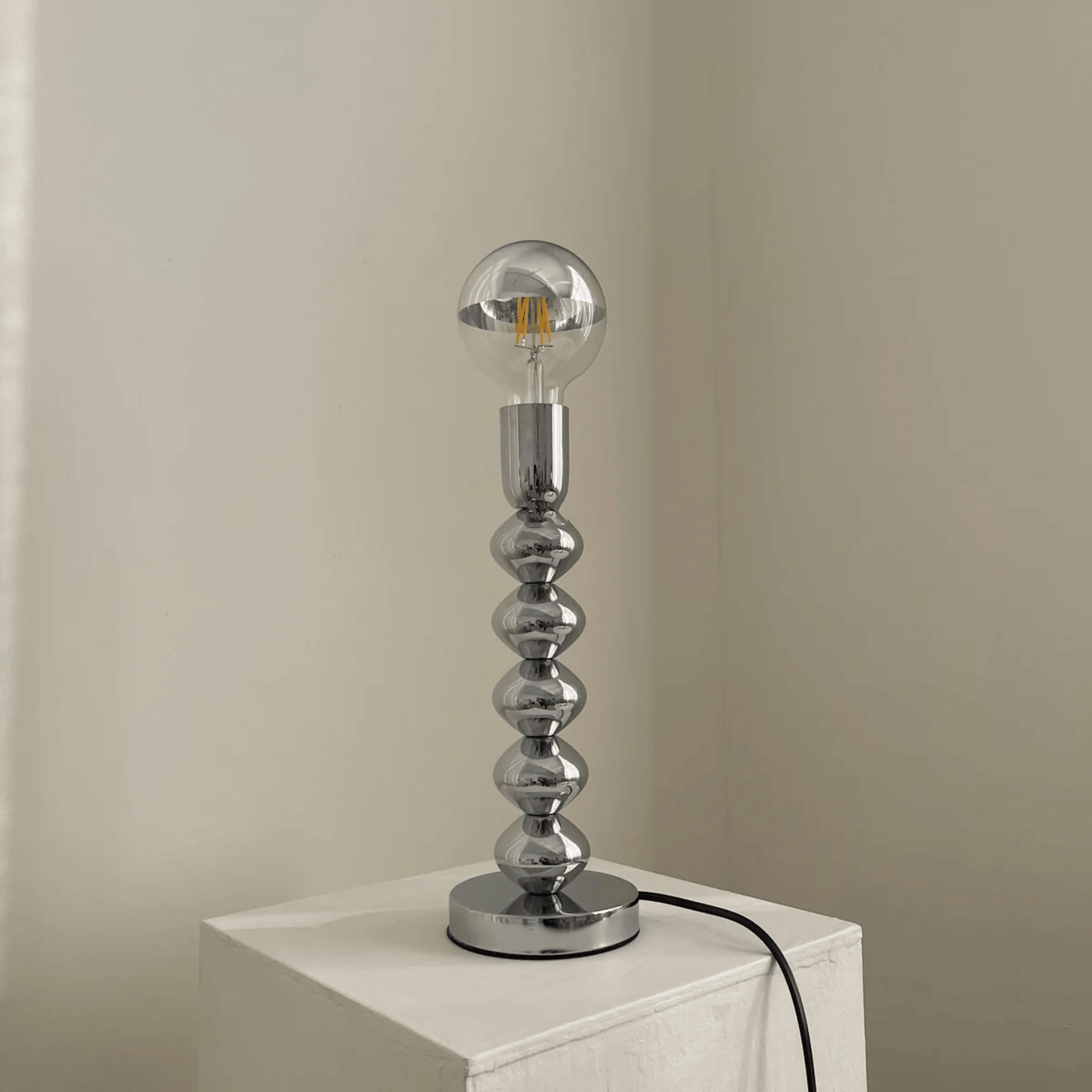 Silver table lamp with a unique design on a white surface against a beige wall.