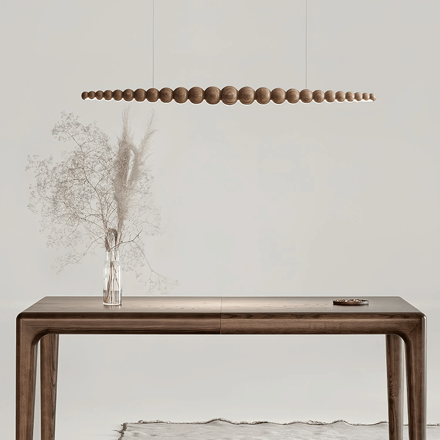 Wooden console table with a vase of dried flowers and a modern pendant light in a minimalistic setting.