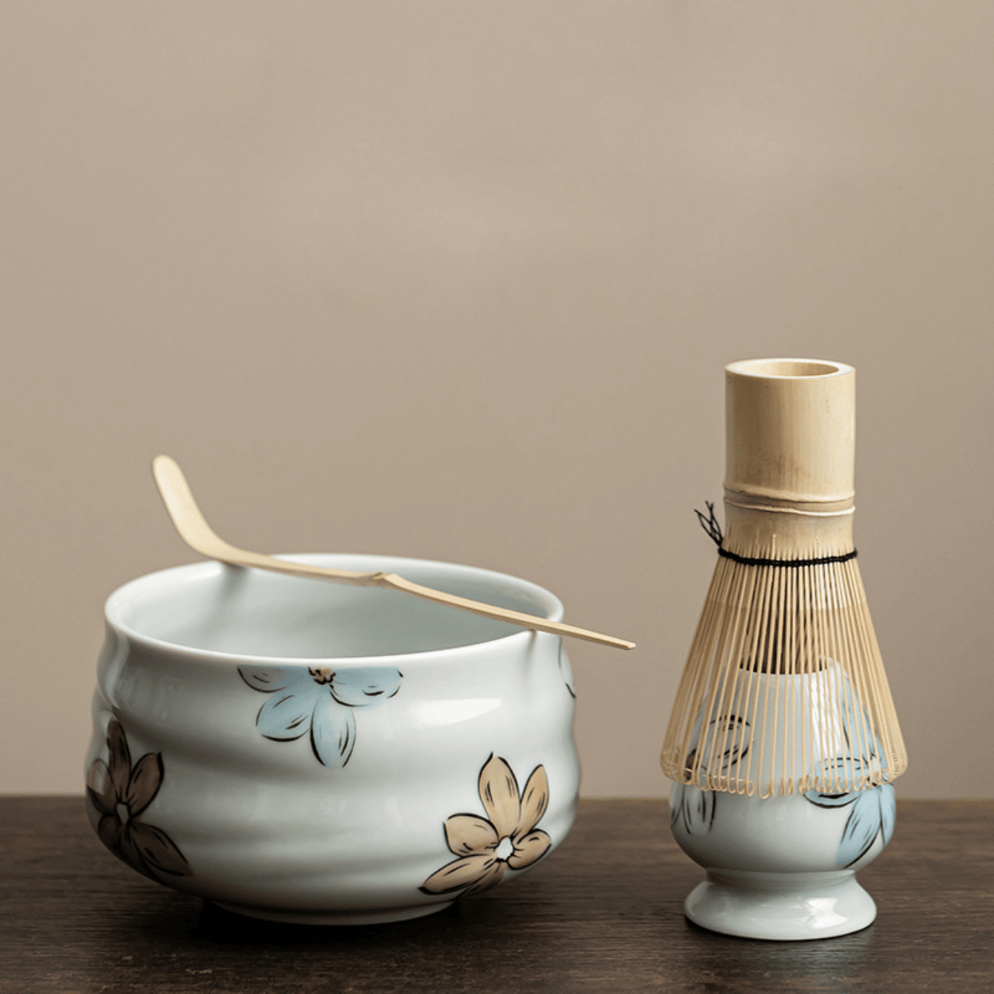 Ceramic bowl with floral designs and a bamboo whisk holder on a wooden surface.