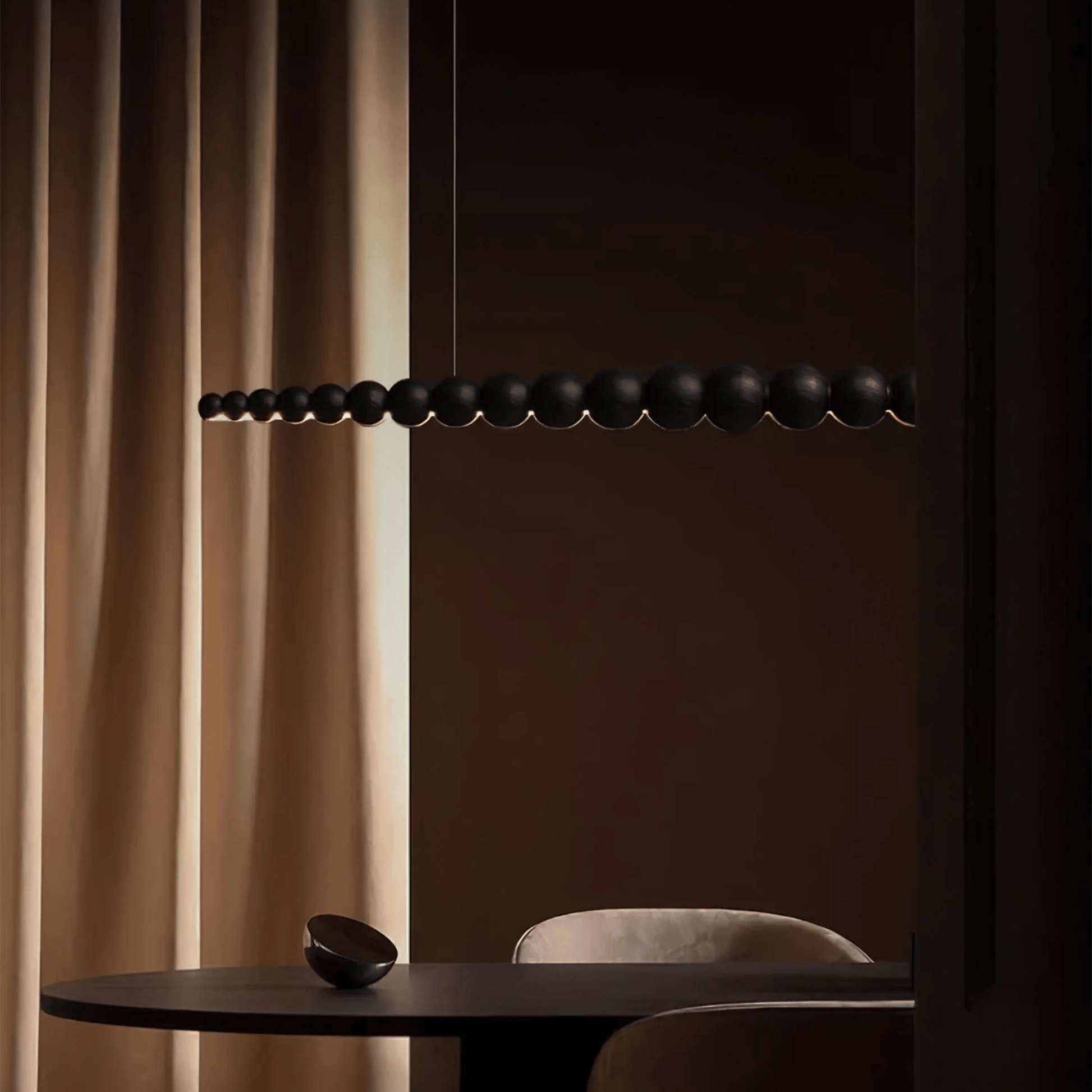 Modern black pendant light fixture against a dark wall with beige curtains.