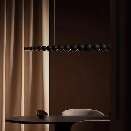 Modern black pendant light fixture against a dark wall with beige curtains.