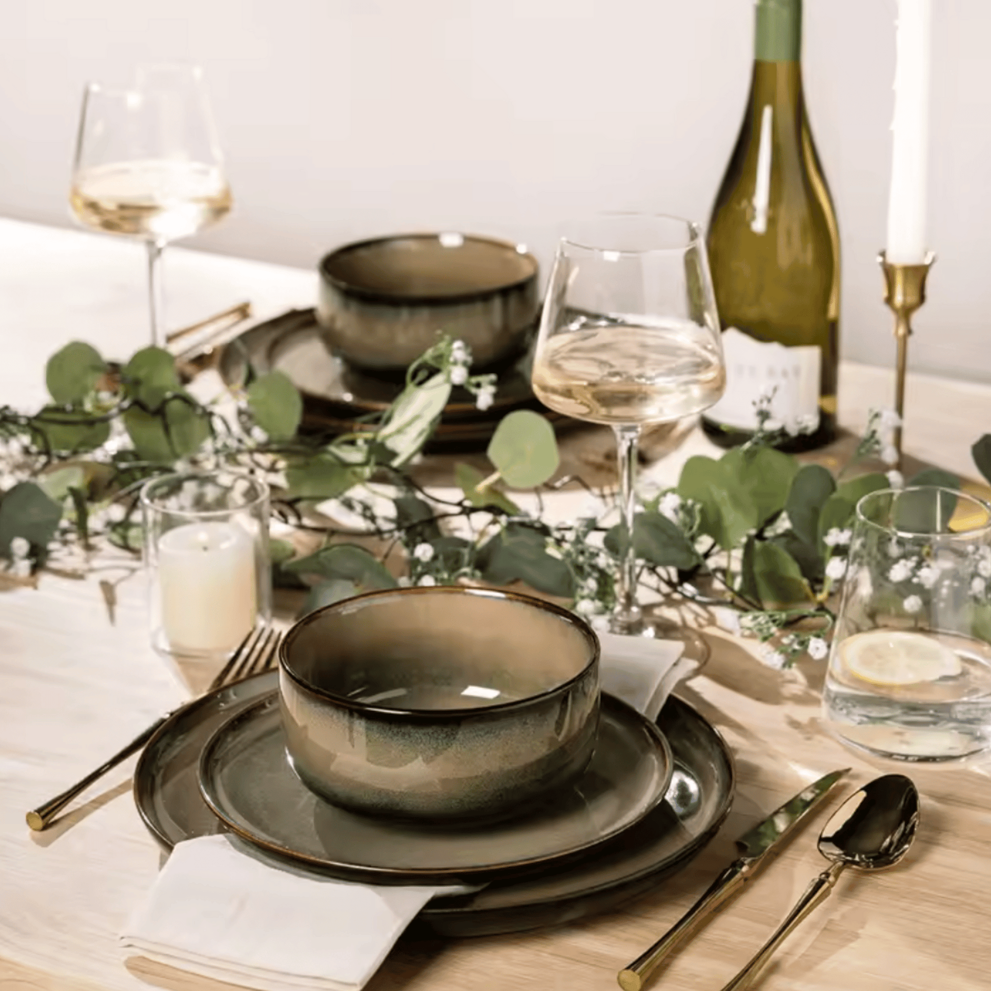 Elegant table setting with green ceramic bowls, wine glasses, and a bottle of white wine.