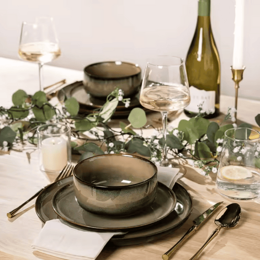 Elegant table setting with green ceramic bowls, wine glasses, and a bottle of white wine.
