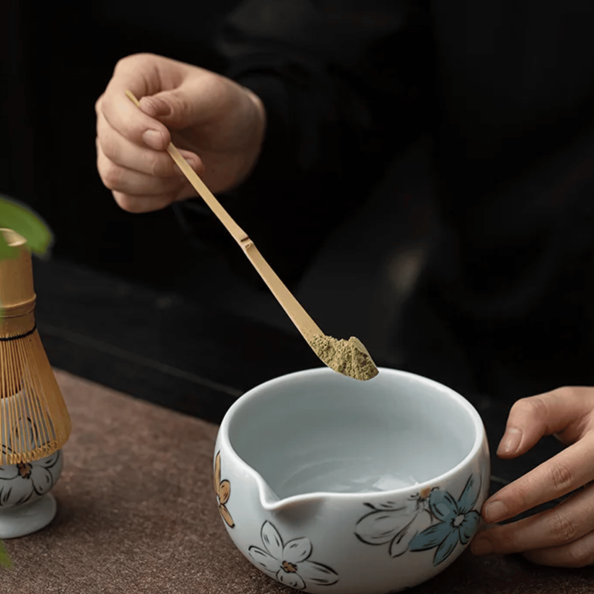 Person preparing tea with a wooden spoon and floral-patterned teacup on a dark background