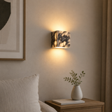 Wall-mounted lamp with marble pattern casting light on a neutral wall, with a vase and plant on a nightstand.