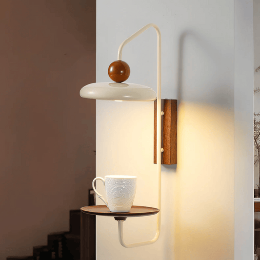 Wall-mounted lamp with a wooden ball and shelf holding a ceramic cup against a neutral wall.