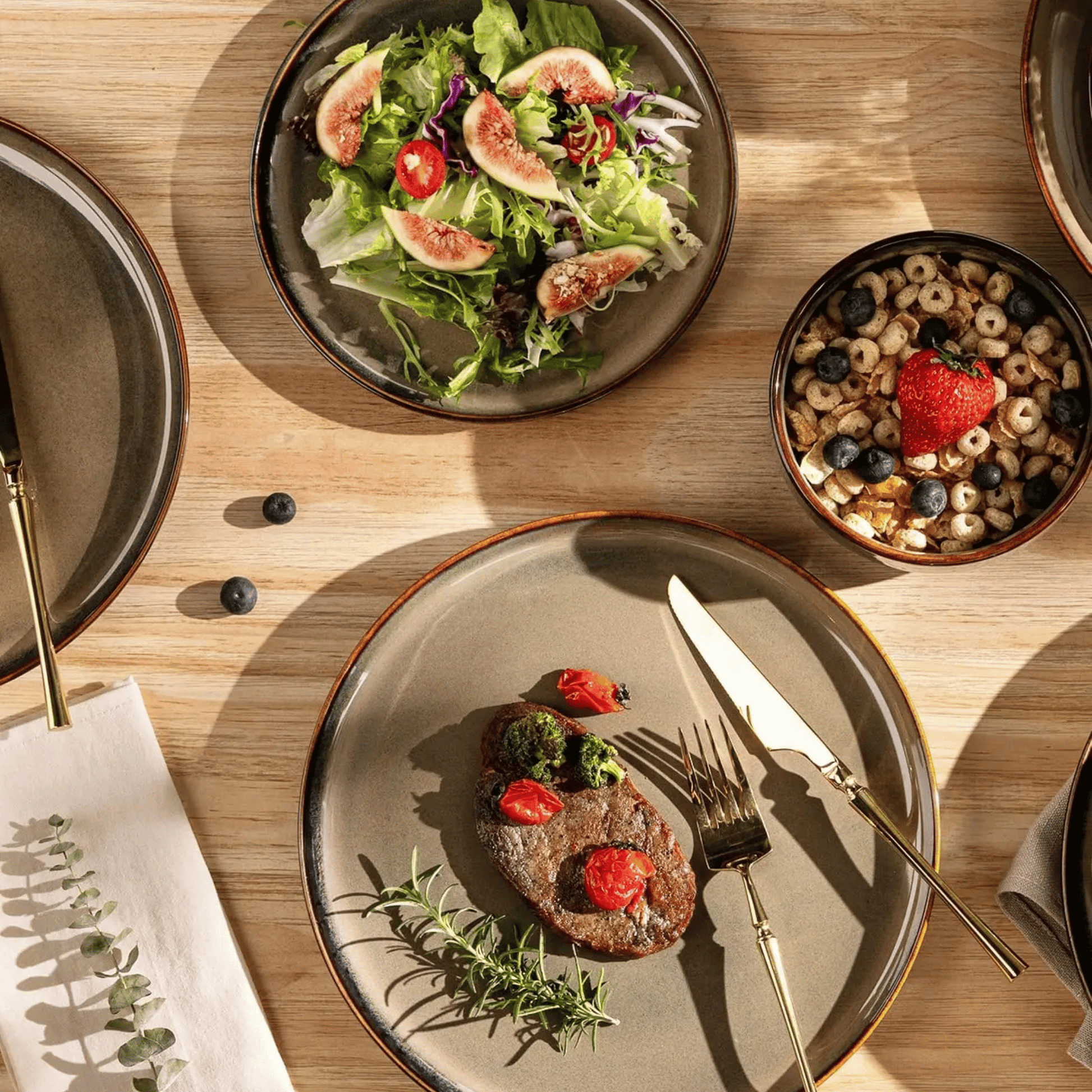 Dinner setting with a plate of food, salad, and a bowl of cereal on a wooden table.