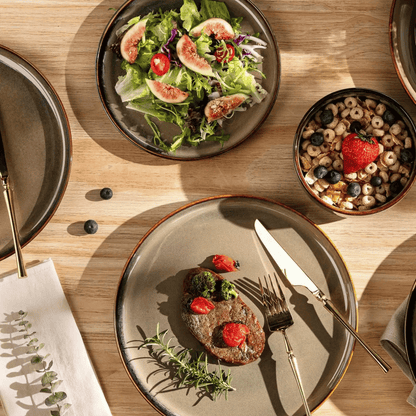Dinner setting with a plate of food, salad, and a bowl of cereal on a wooden table.