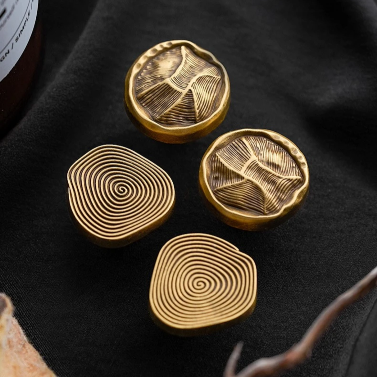 Four gold coasters with unique patterns on a black surface