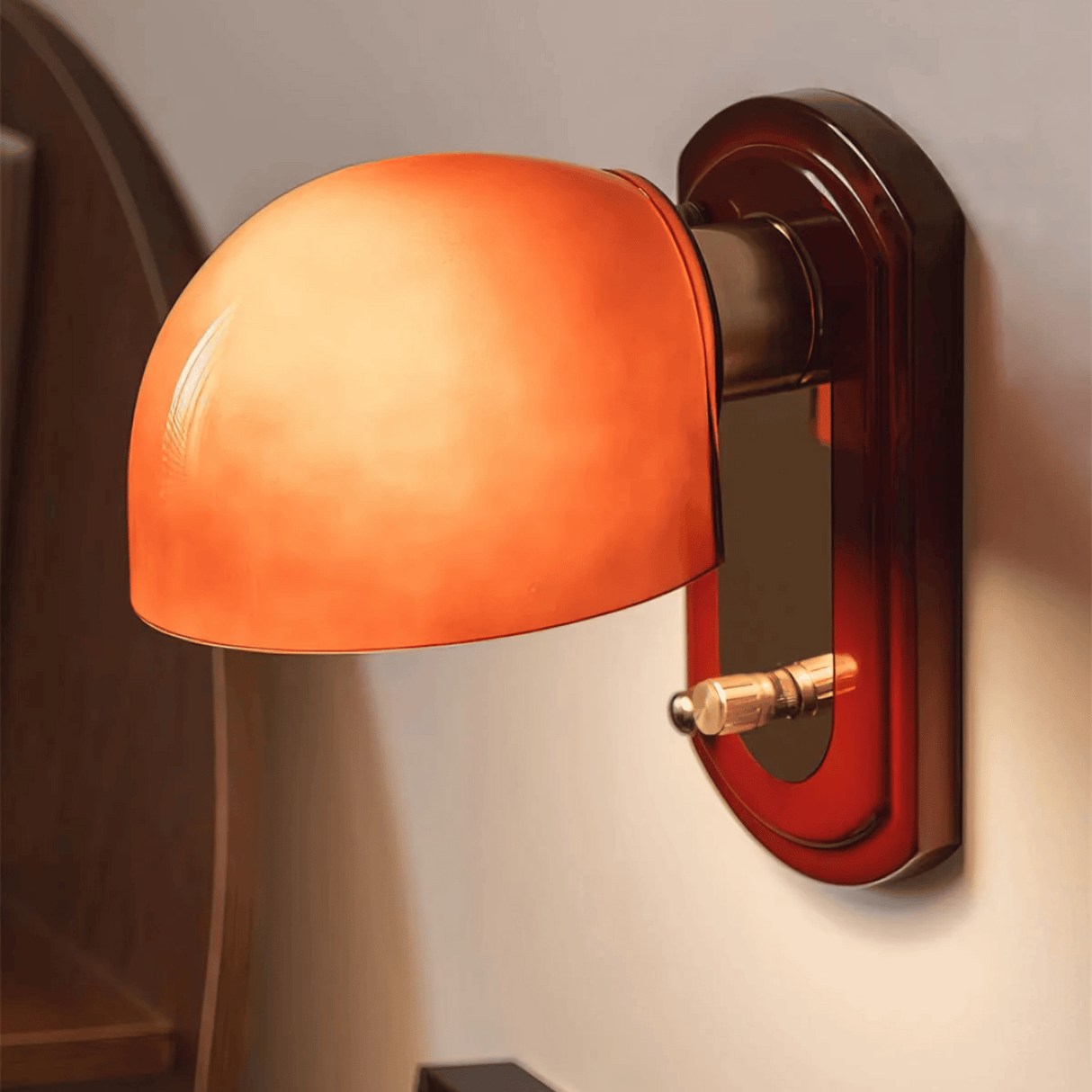 Wall-mounted lamp with orange glass shade and brown metal fixture on a neutral wall.