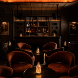 Dark, cozy lounge with brown chairs, dim lighting, and a shelf with records.