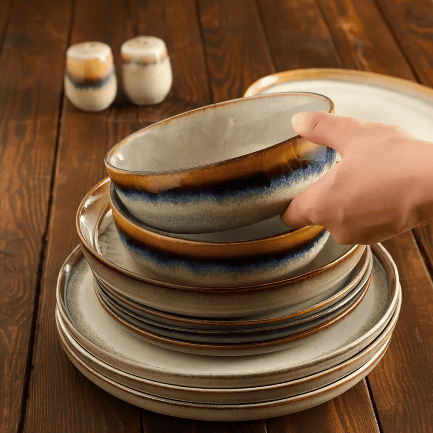 Stack of ceramic plates with a hand reaching for one on a wooden table