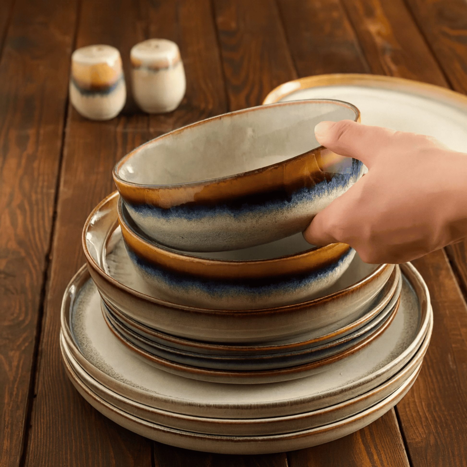 Stack of ceramic plates with a hand reaching for one on a wooden table