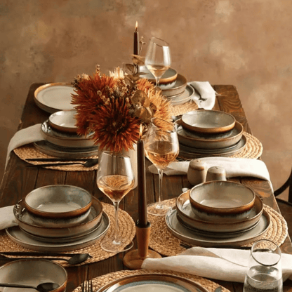 Elegant table setting with ceramic plates, glasses, and a floral centerpiece on a wooden table.