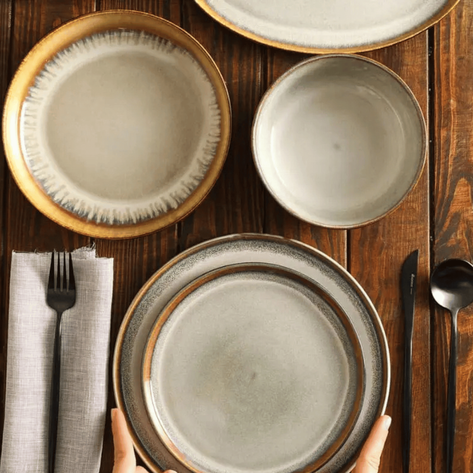 Set of ceramic plates on a wooden table with cutlery and napkin.