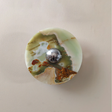 Round green and brown marbled stone with a silver button in the center on a beige background
