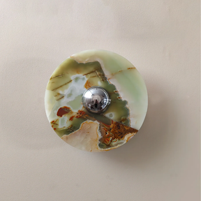 Round green and brown marbled stone with a silver button in the center on a beige background