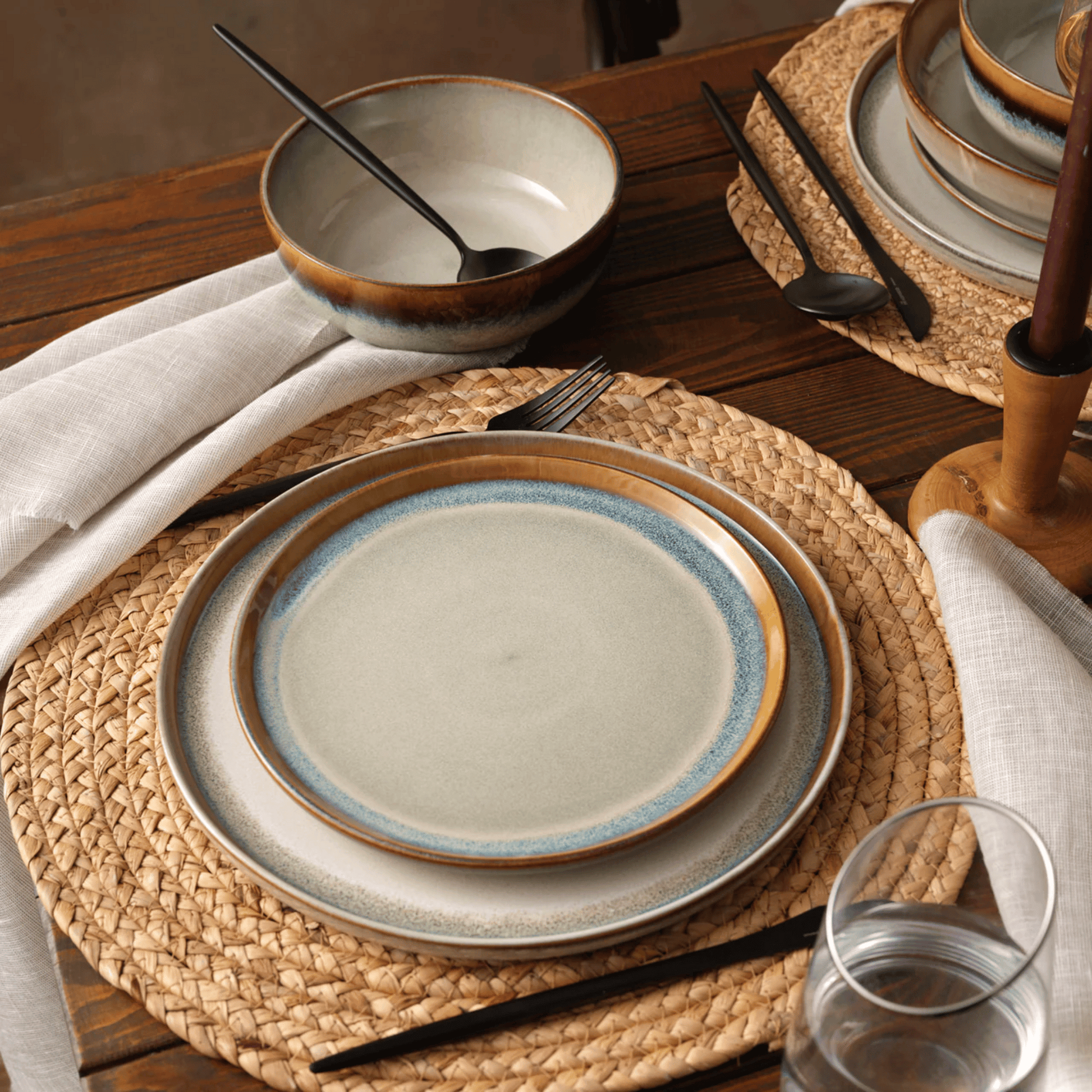 Ceramic plates and bowls on a wooden table with woven placemats.