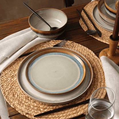 Ceramic plates and bowls on a wooden table with woven placemats.