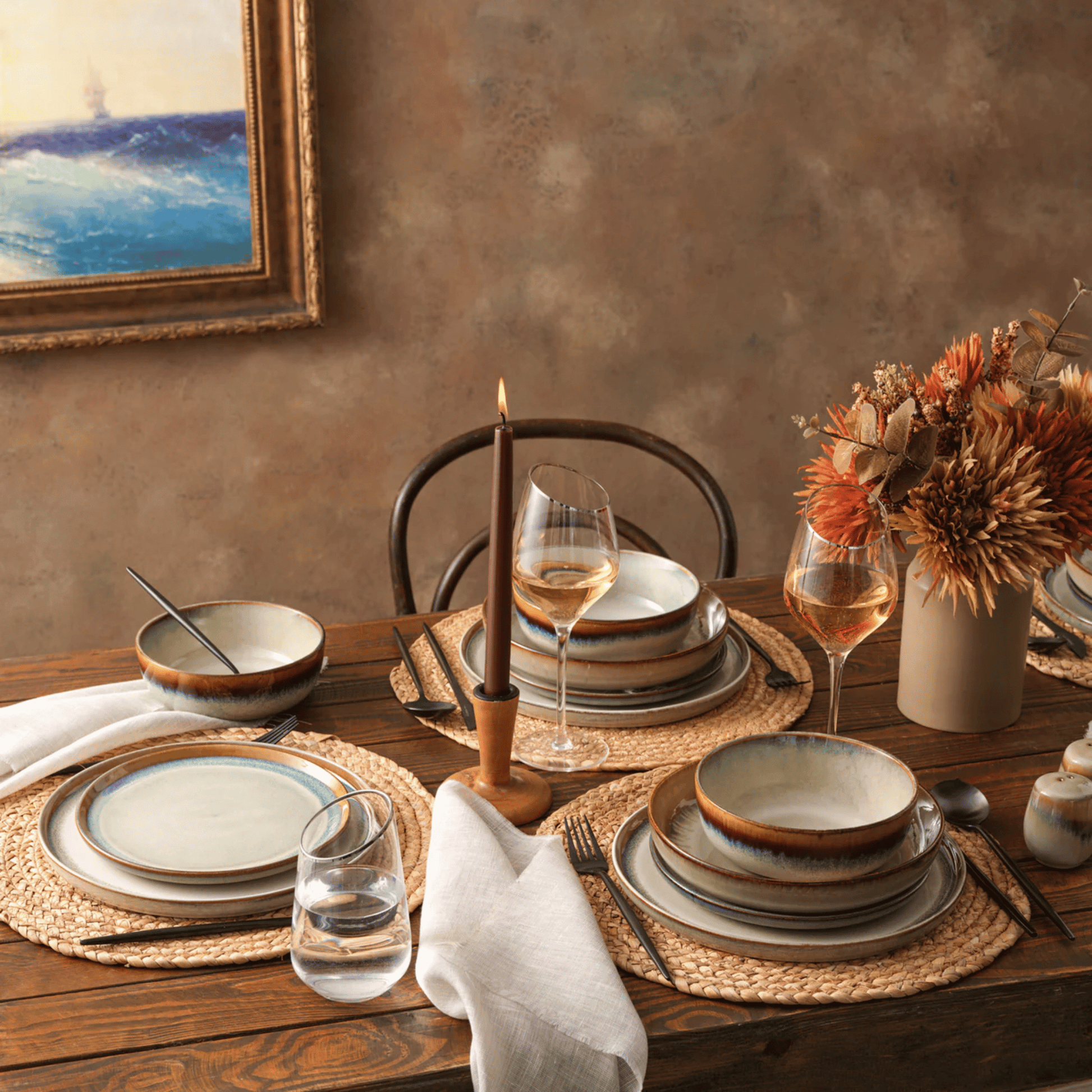 Dining table setting with ceramic plates, glasses, and a candle on a wooden table.
