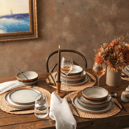 Dining table setting with ceramic plates, glasses, and a candle on a wooden table.