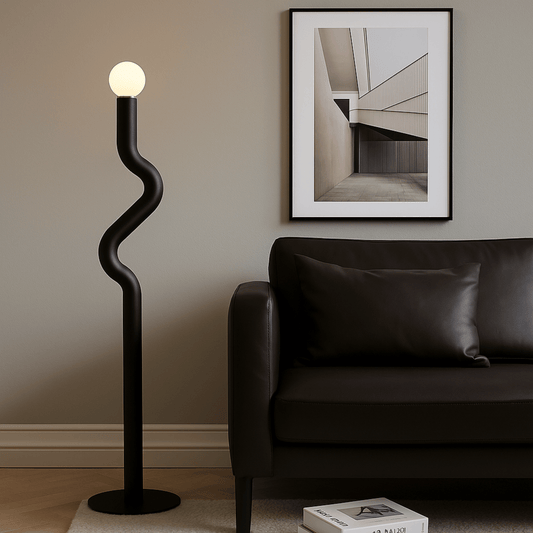Modern black floor lamp in a living room with a sofa and framed artwork on the wall.