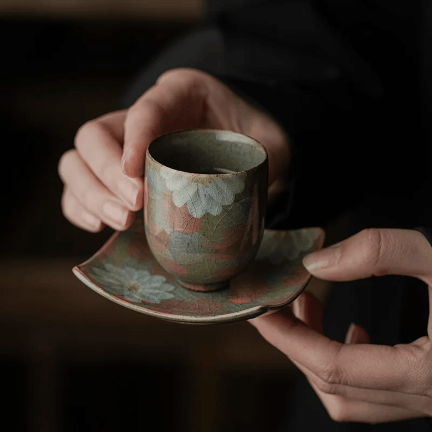 Person holding a ceramic cup and saucer with floral patterns