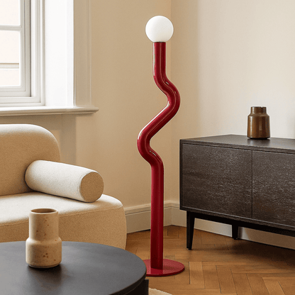 Modern red floor lamp in a living room setting with a beige armchair and wooden sideboard.