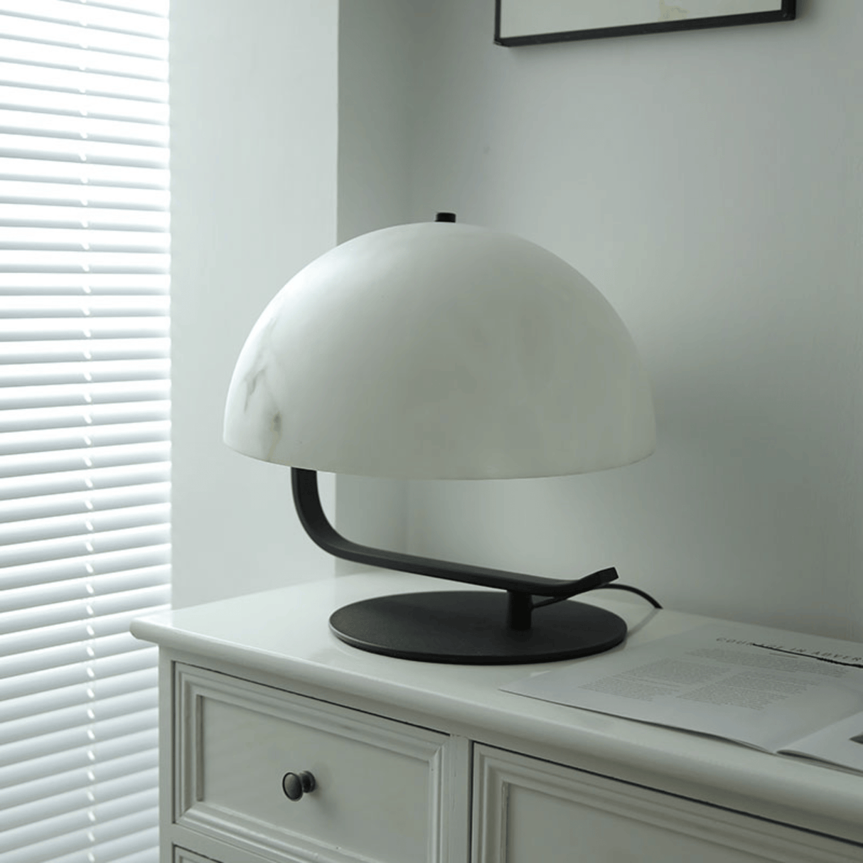White table lamp on a white dresser with blinds in the background