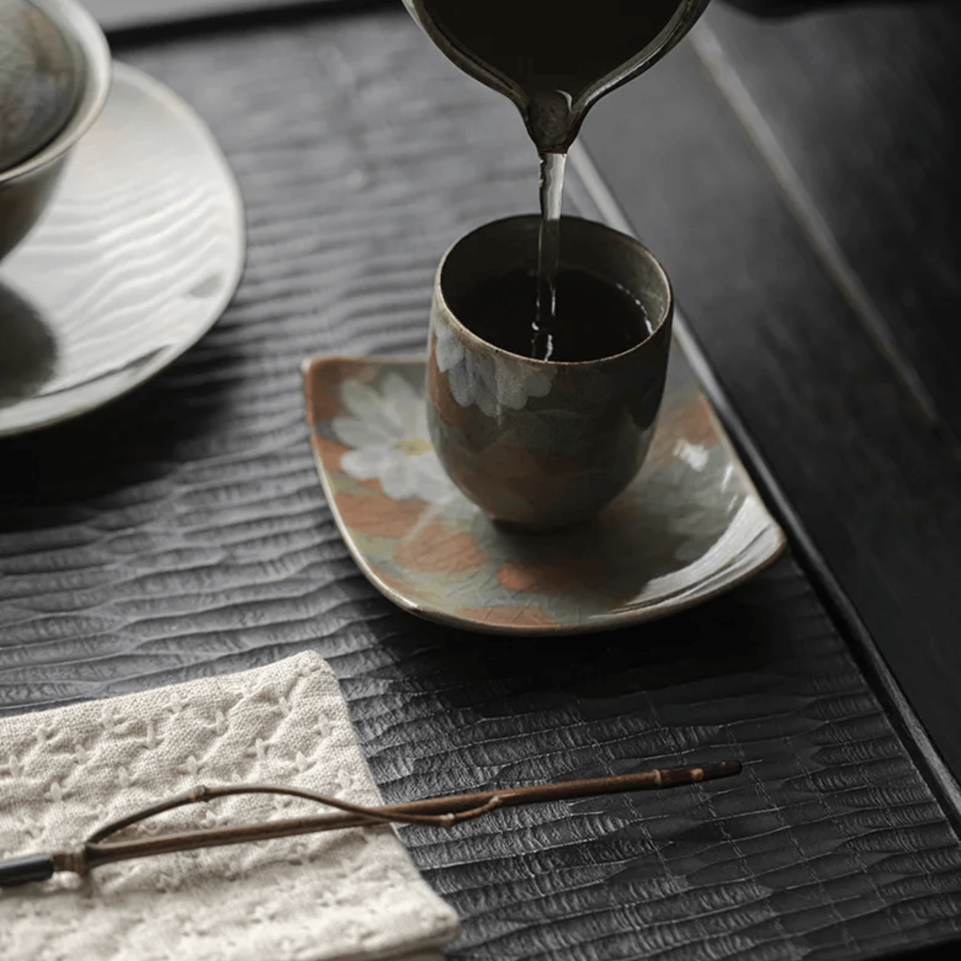 Tea being poured from a teapot into a cup on a textured surface.