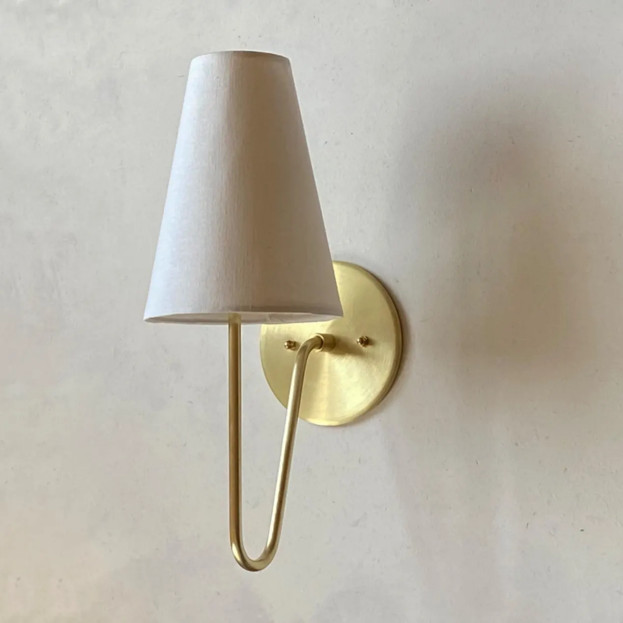 Wall-mounted lamp with a white shade and gold fixture on a light beige wall.