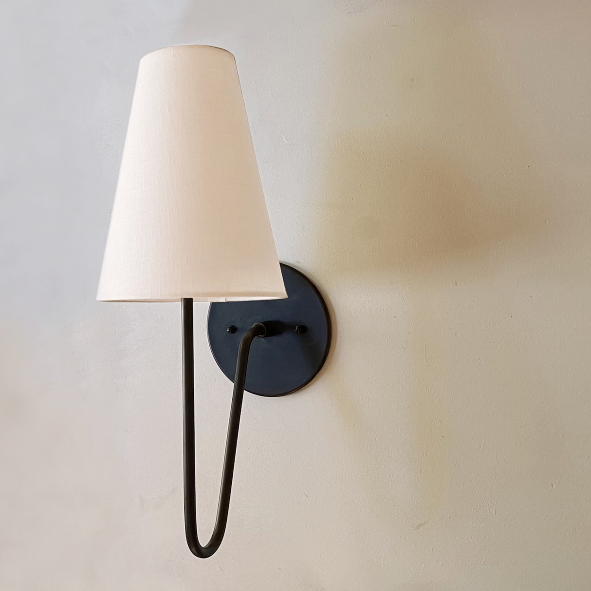 Wall-mounted lamp with a white shade and black metal arm on a light gray wall.