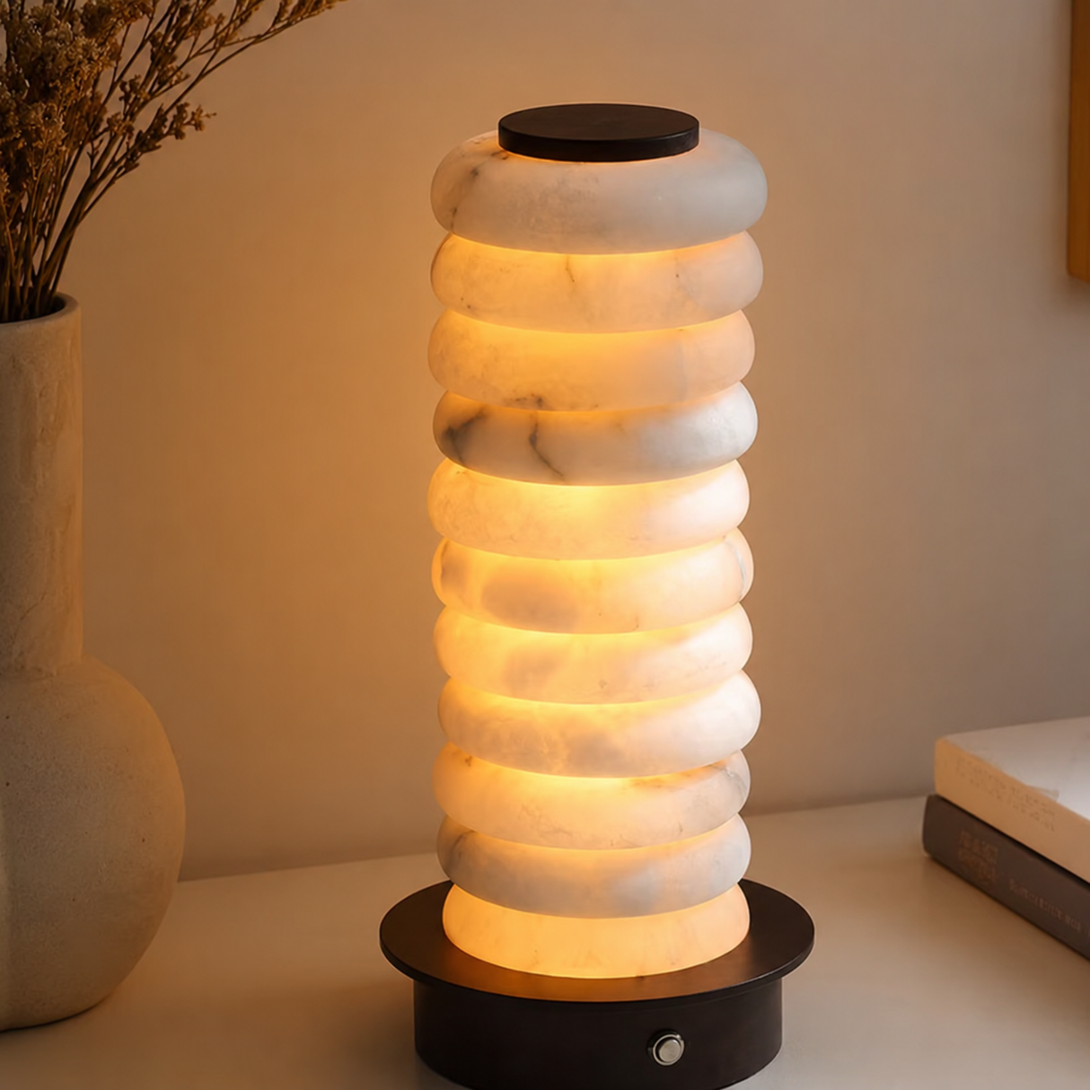 Decorative lamp with marble-like texture on a table next to a vase with dried flowers.