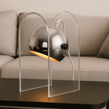 Modern table lamp with clear acrylic base on a wooden surface, blurred sofa in the background