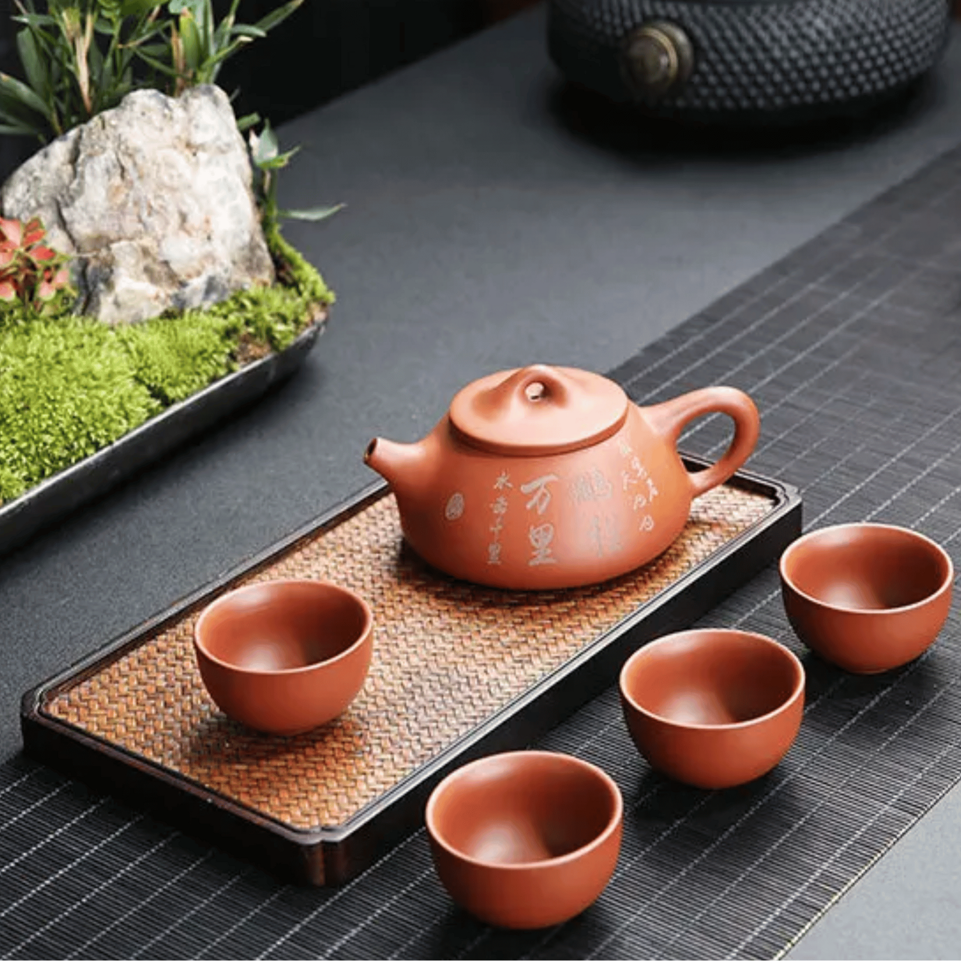 Tea set with a teapot and four cups on a woven tray.