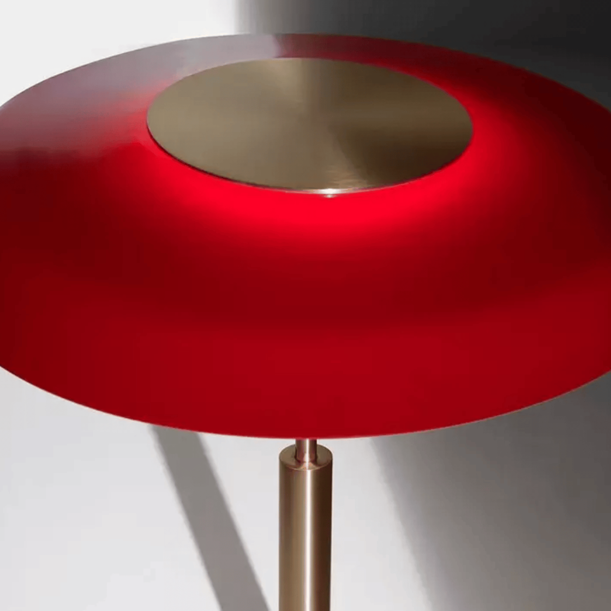 Modern side table with red circular top and bronze base on a white background