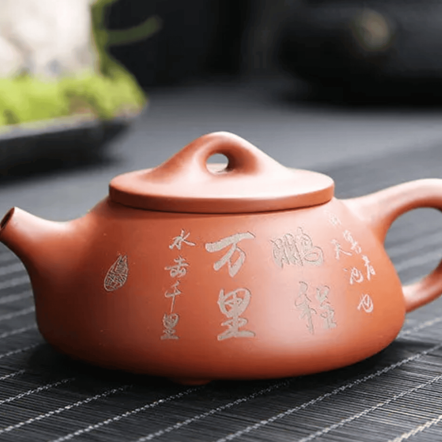 Red clay teapot with Chinese characters on a dark surface