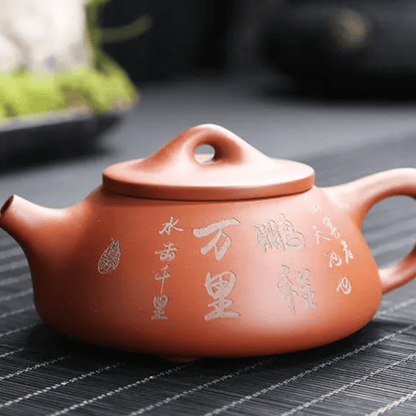 Red clay teapot with Chinese characters on a dark surface