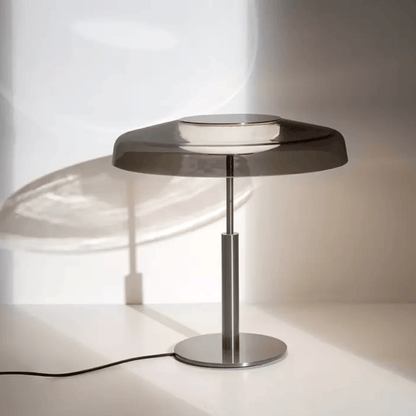 Modern table lamp with a metallic base and glass shade on a white surface.