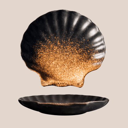 Black shell-shaped dish with gold interior on a beige background