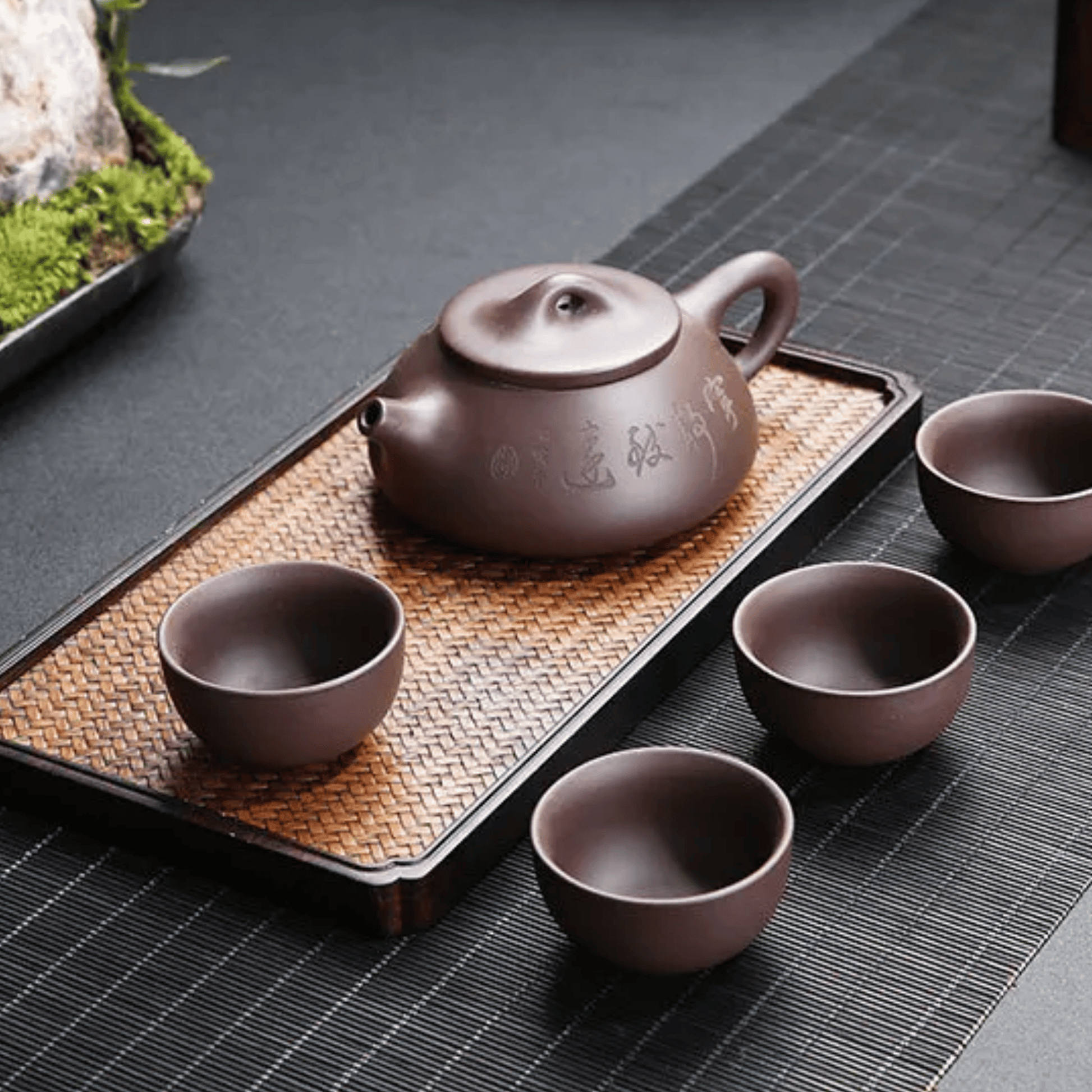Tea set with a teapot and four cups on a woven tray.