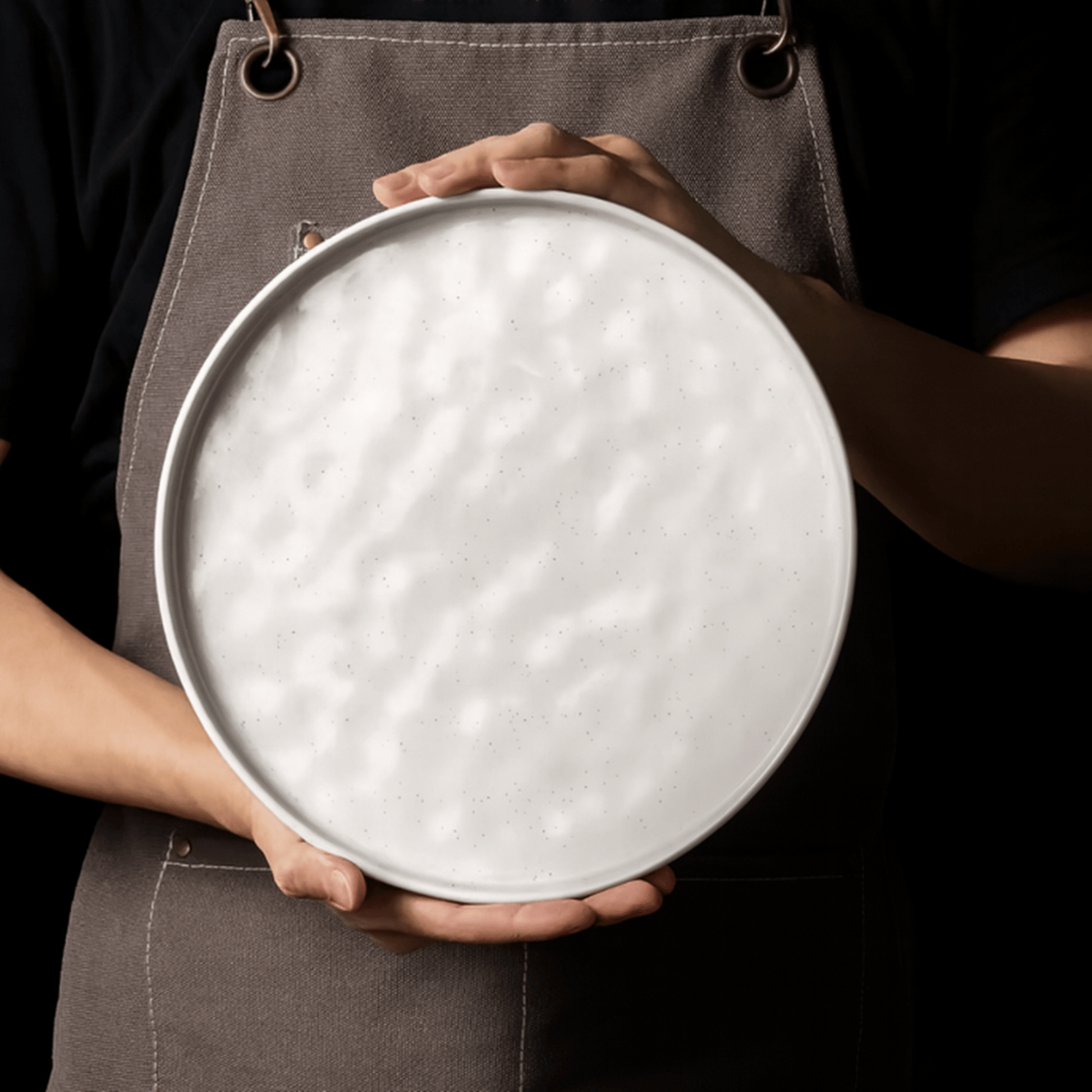 Person holding a round metal tray with a textured surface against a dark background