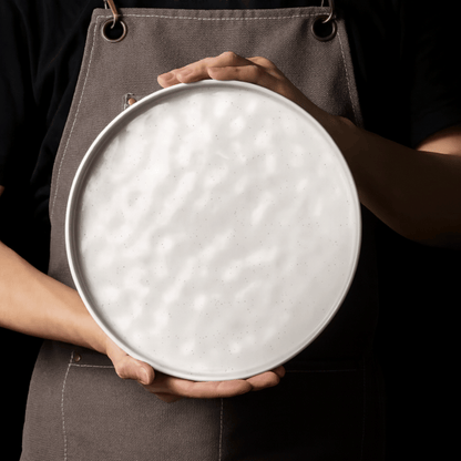 Person holding a round metal tray with a textured surface against a dark background