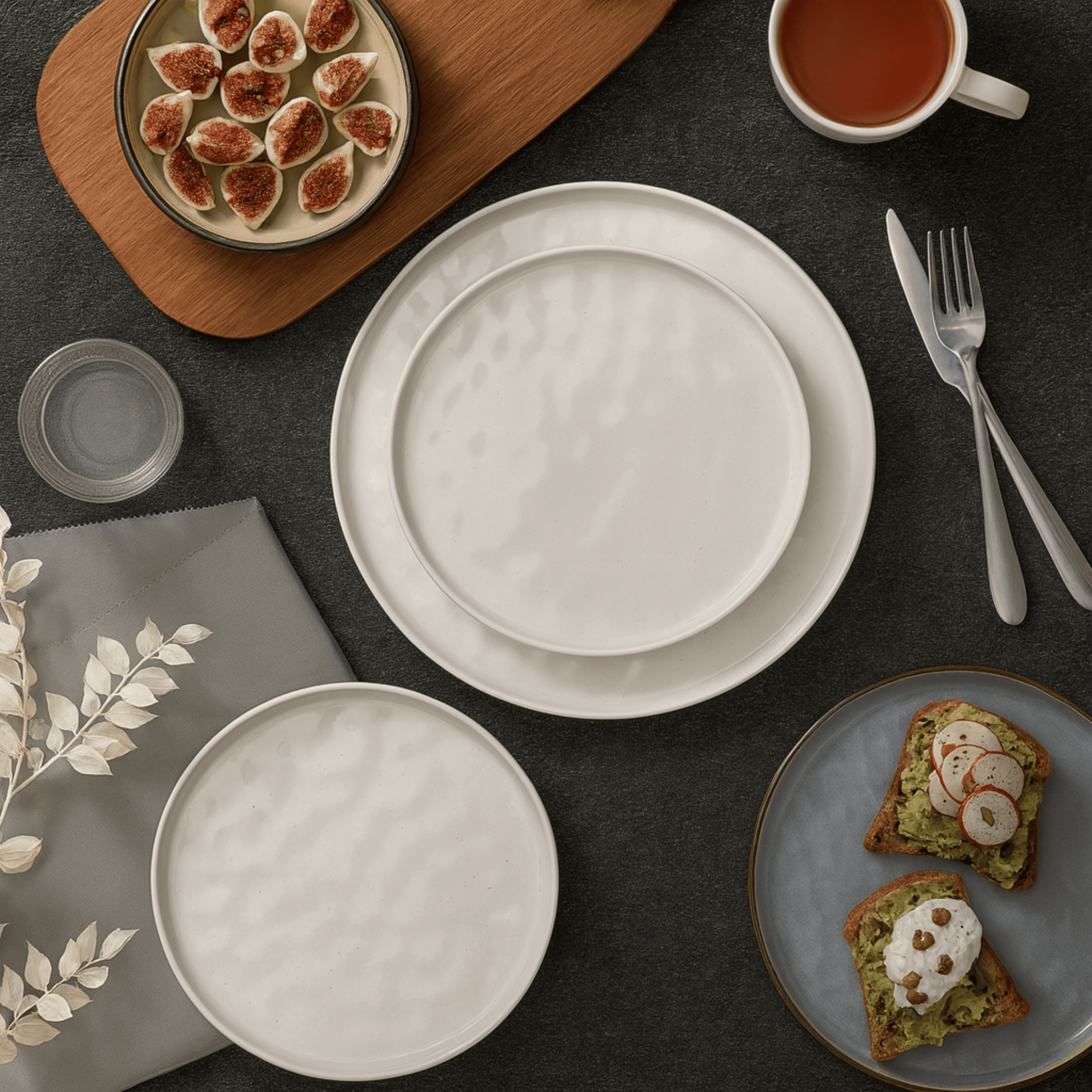Table setting with white plates, a cup of tea, and a plate of toast with avocado spread.
